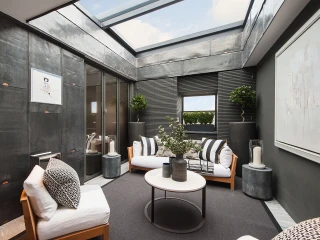 Un espace intérieur moderne avec des murs en métal et des grandes fenêtres laissant entrer la lumière. Deux canapé blancs entourent une table basse ronde. Des plantes et des décorations minimalistes ajoutent une touche de verdure.