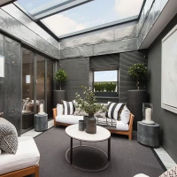 Un espace intérieur moderne avec des murs en métal et des grandes fenêtres laissant entrer la lumière. Deux canapé blancs entourent une table basse ronde. Des plantes et des décorations minimalistes ajoutent une touche de verdure.