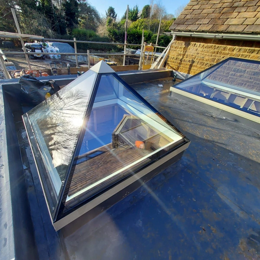 Un tetraedre de vitre sur un tetto, reflectent la construccione ad proximitate. Arbori verd et costruccions se vident in fondo.