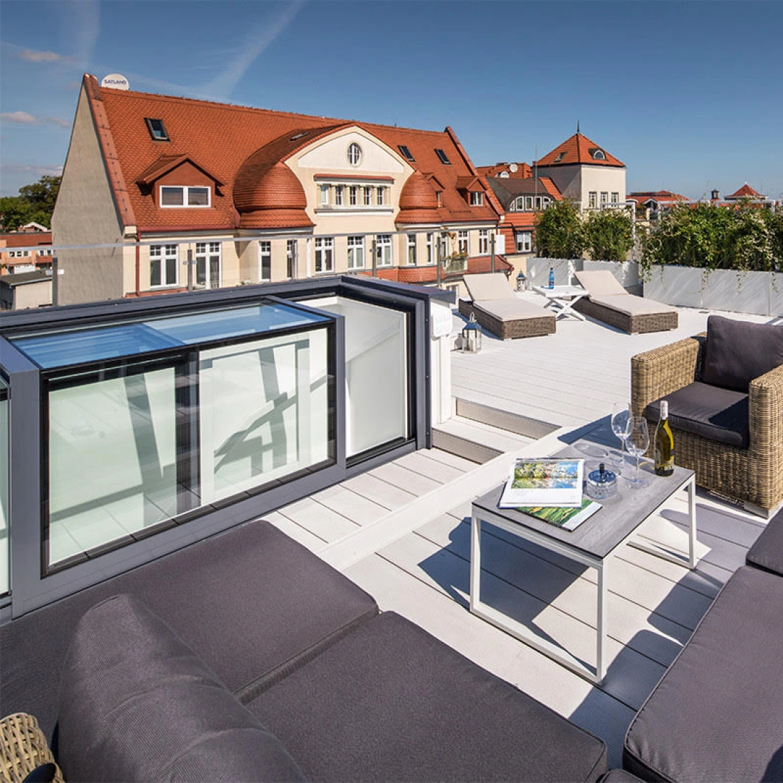 Terrasse moderne avec des canapés en rotin, une table basse et une vue sur un bâtiment de style architecture classique et la ville en arrière-plan. Le ciel est dégagé et ensoleillé.