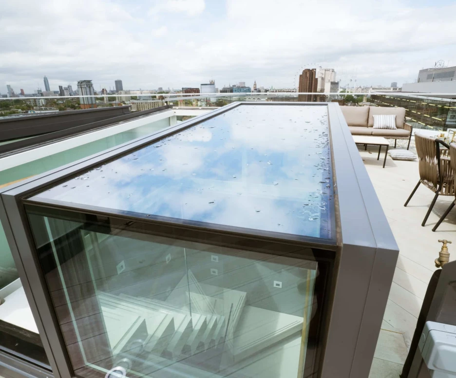 A glass-top terrace entrance with a view of a city skyline in the background. The rooftop area features modern seating and greenery.