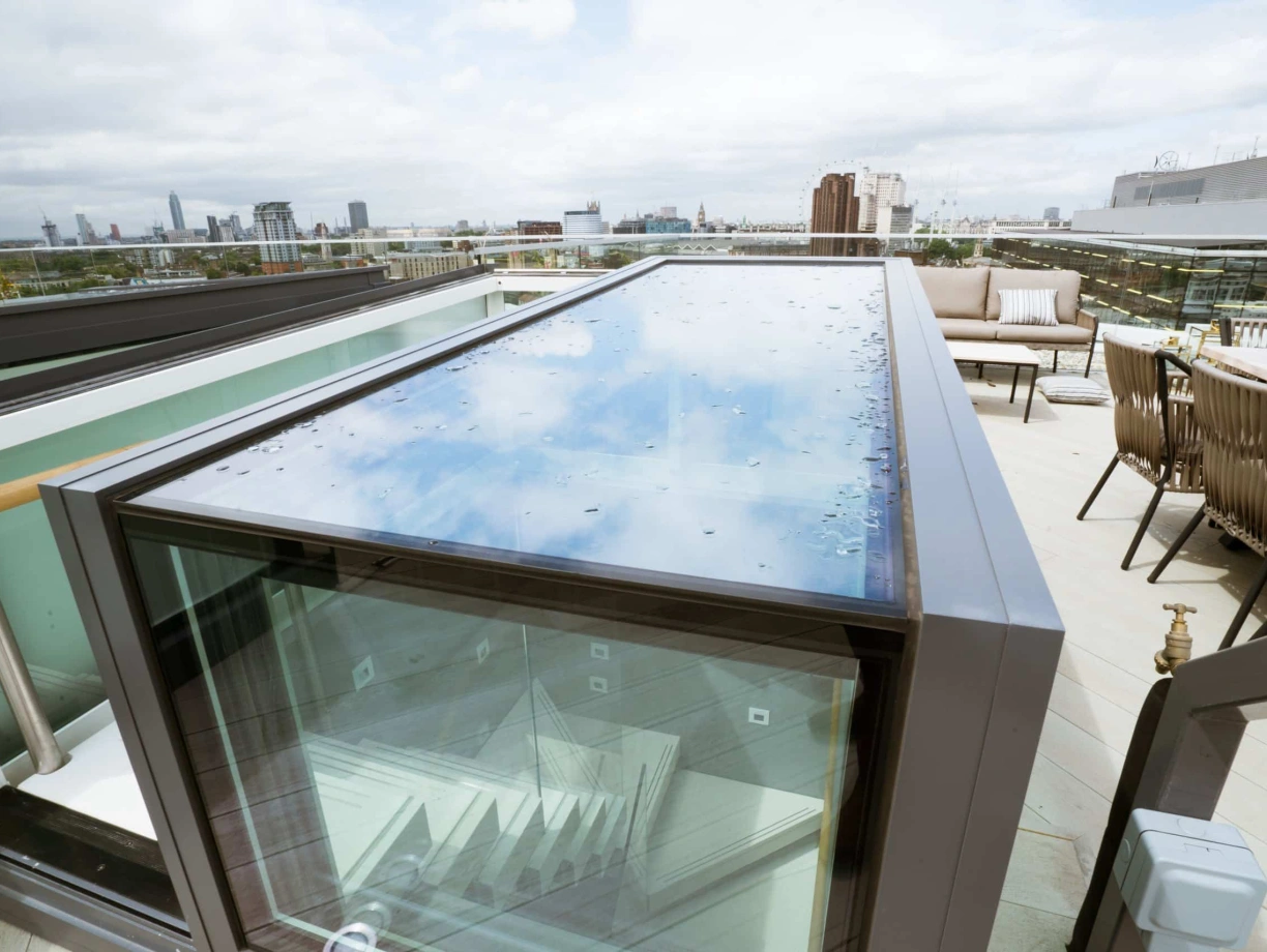 A glass-top terrace entrance with a view of a city skyline in the background. The rooftop area features modern seating and greenery.