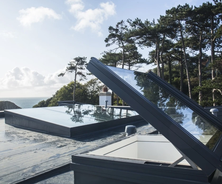 Skylights open on a flat roof, overlooking a scenic view of trees and the ocean under a partly cloudy sky.