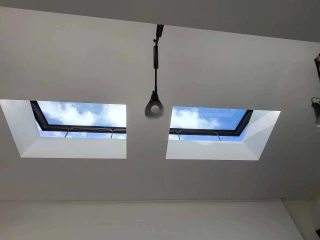 Two skylights in a white ceiling, showing a blue sky with scattered clouds. A single pendant light hangs below one of the skylights.