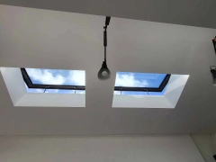 Two skylights in a white ceiling, showing a blue sky with scattered clouds. A single pendant light hangs below one of the skylights.