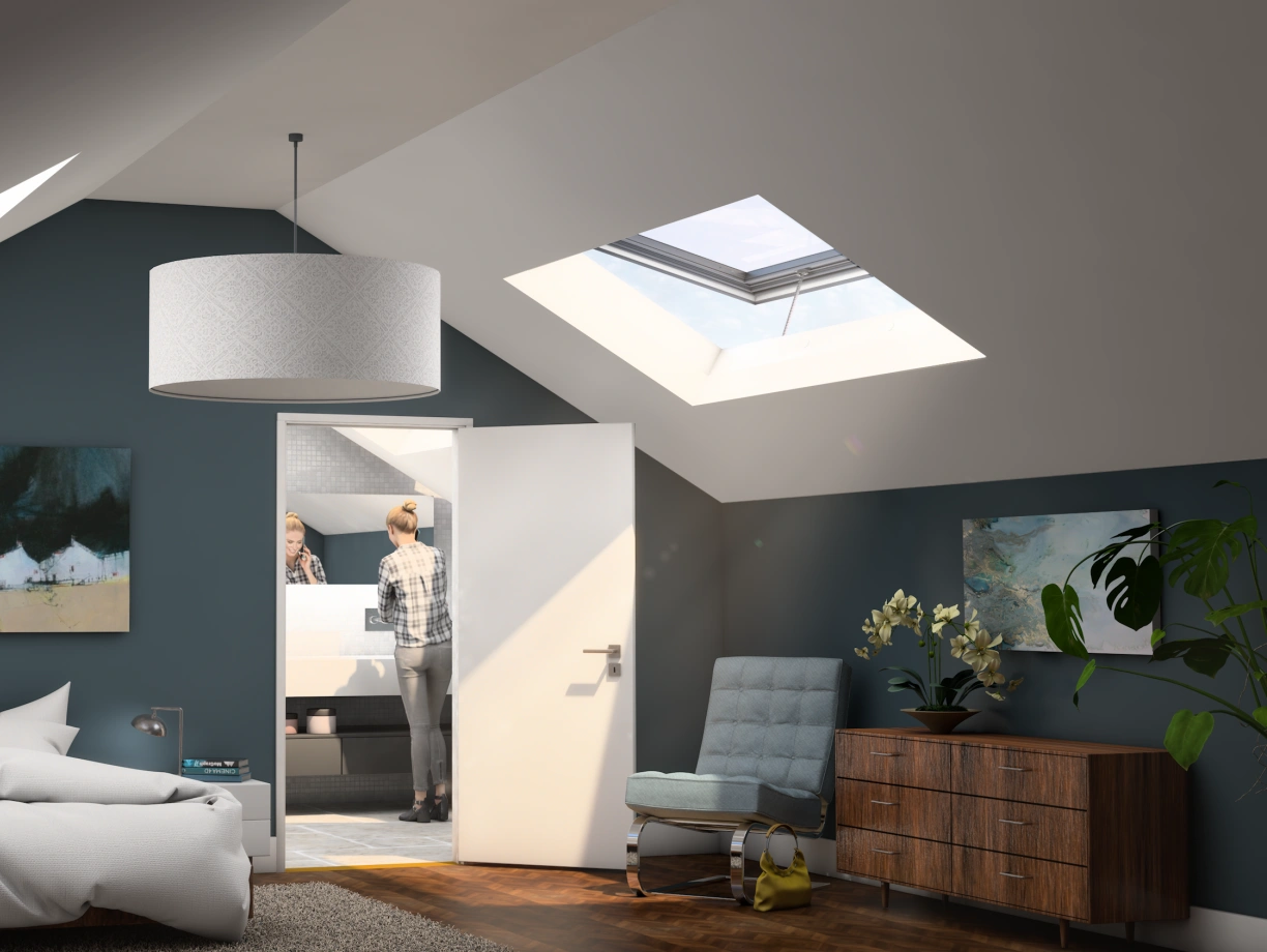 Chambre mansardée avec un grand lit en désordre, des murs bleu foncé, une œuvre d’art moderne accrochée, et une porte ouverte menant à une salle de bain. Un homme se tient devant un lavabo, tandis qu’un lampadaire et une plante décorent l’espace.