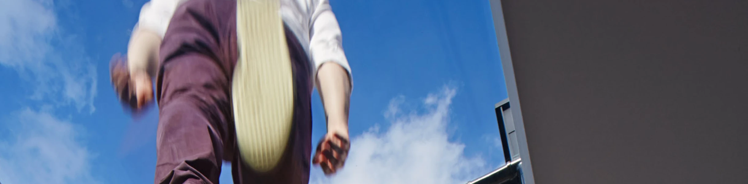 A person is seen walking on a glass skylight, with their feet visible above a brick building. The blue sky peeks through the skylight.