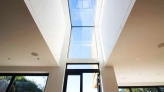 Bright modern interior featuring a large skylight that brings natural light into the space. The view through the skylight shows a clear blue sky. Large glass doors open to a green outdoor area.