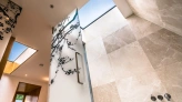A modern bathroom featuring large, marble tiles and a frosted glass door with a floral design. Natural light streams in through skylights, illuminating the space.